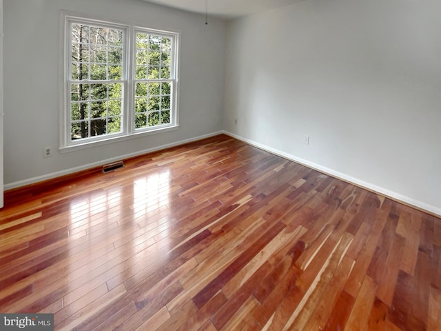 empty room featuring visible vents, baseboards, and wood-type flooring