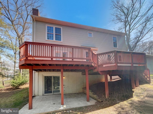 back of property with brick siding, a wooden deck, a chimney, and a patio