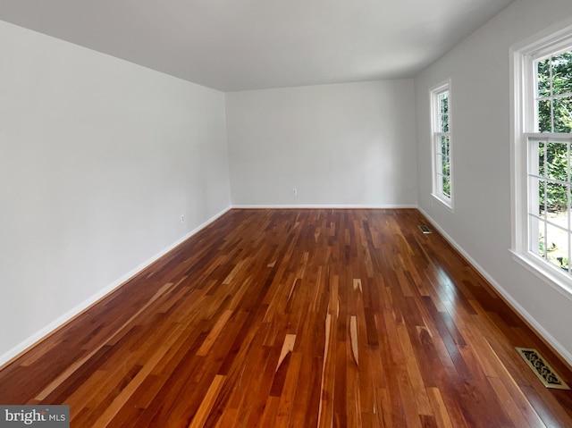 spare room featuring visible vents, baseboards, a healthy amount of sunlight, and dark wood-style flooring