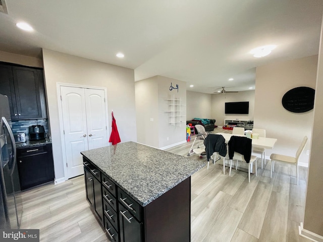 kitchen featuring stone countertops, a center island, freestanding refrigerator, light wood finished floors, and ceiling fan