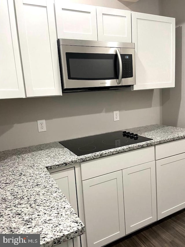 kitchen featuring white cabinetry, stainless steel microwave, black electric cooktop, and dark wood finished floors