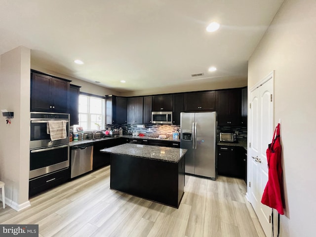 kitchen featuring dark stone countertops, a kitchen island, light wood-style flooring, appliances with stainless steel finishes, and backsplash