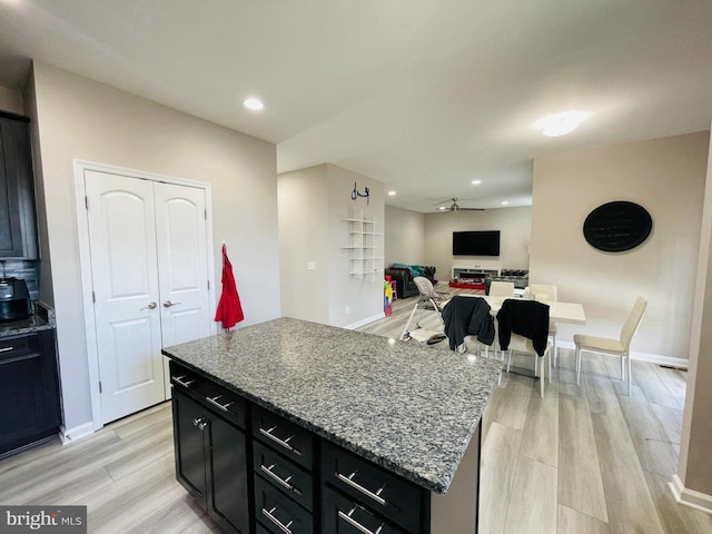 kitchen with light wood finished floors, a kitchen island, dark cabinetry, and ceiling fan