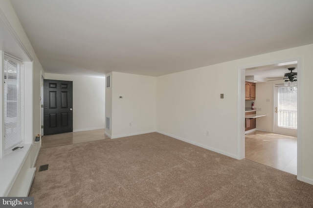 empty room with visible vents, light carpet, baseboards, and a ceiling fan