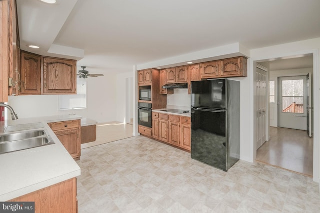 kitchen with under cabinet range hood, light countertops, brown cabinets, black appliances, and a sink