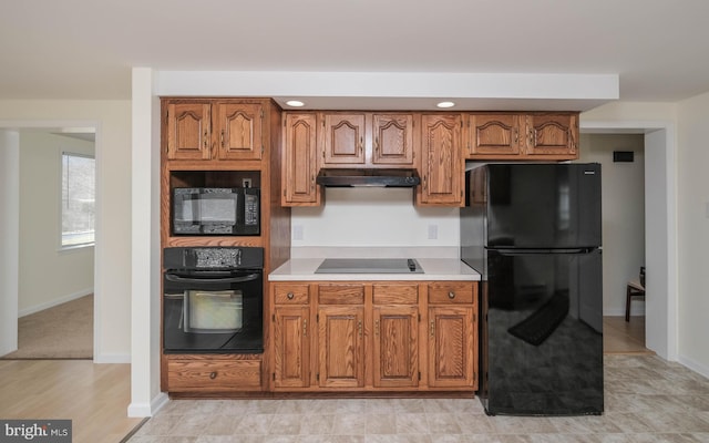 kitchen featuring under cabinet range hood, black appliances, and brown cabinetry