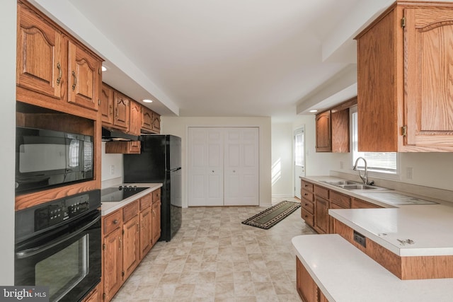 kitchen featuring under cabinet range hood, light countertops, brown cabinets, black appliances, and a sink