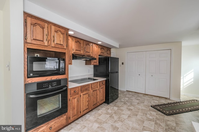 kitchen featuring baseboards, under cabinet range hood, light countertops, brown cabinets, and black appliances