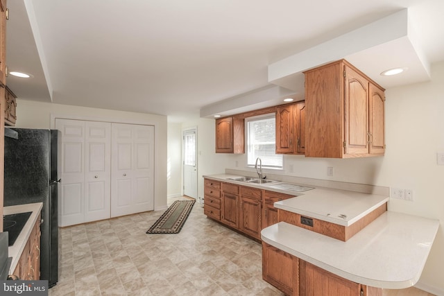 kitchen featuring a sink, recessed lighting, a peninsula, brown cabinetry, and light countertops