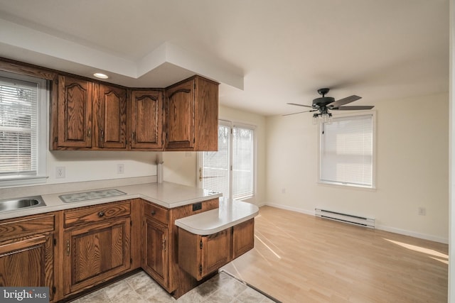 kitchen with baseboards, a peninsula, ceiling fan, light countertops, and baseboard heating