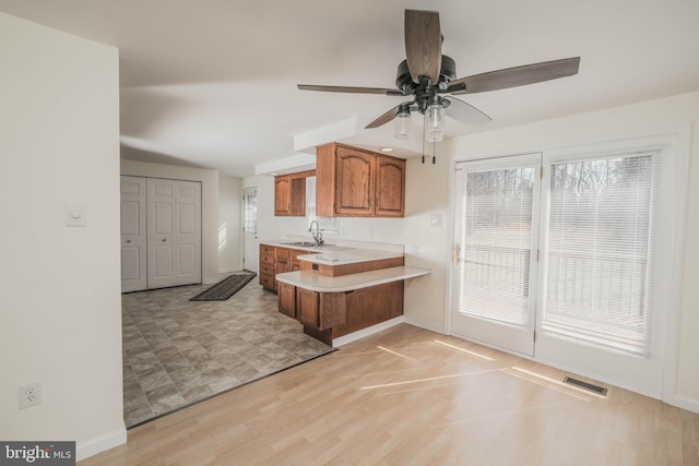 kitchen with a ceiling fan, brown cabinetry, visible vents, a peninsula, and light countertops