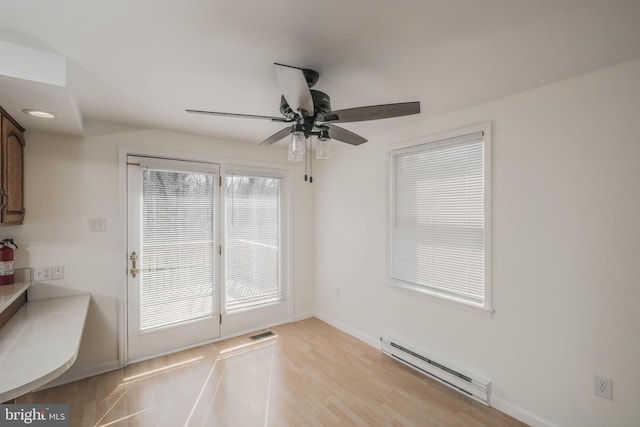 unfurnished dining area featuring visible vents, light wood-style flooring, a baseboard heating unit, baseboards, and ceiling fan