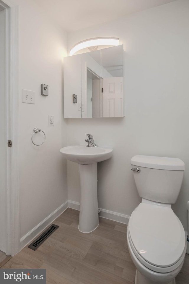 half bath featuring visible vents, baseboards, toilet, and wood finished floors