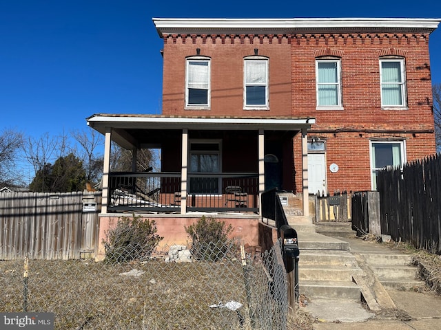 view of front of house featuring brick siding, covered porch, and fence