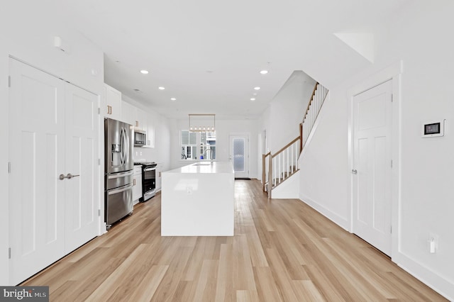 kitchen featuring a center island with sink, stainless steel appliances, light countertops, white cabinets, and light wood-style floors