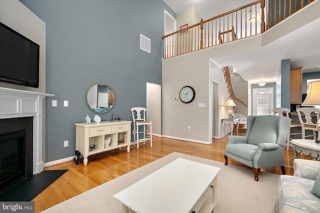 living area featuring a glass covered fireplace, visible vents, baseboards, and wood finished floors