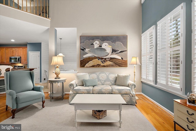 living area with recessed lighting, baseboards, light wood-style floors, and a towering ceiling