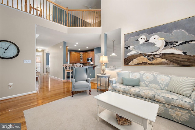 living room with light wood-type flooring, baseboards, and a towering ceiling