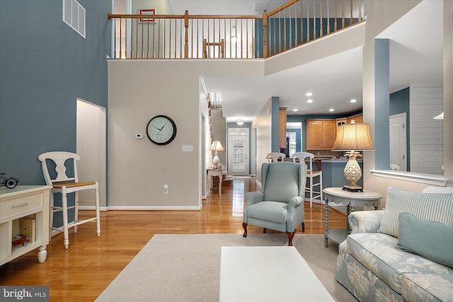 living area featuring baseboards, visible vents, light wood finished floors, recessed lighting, and a towering ceiling