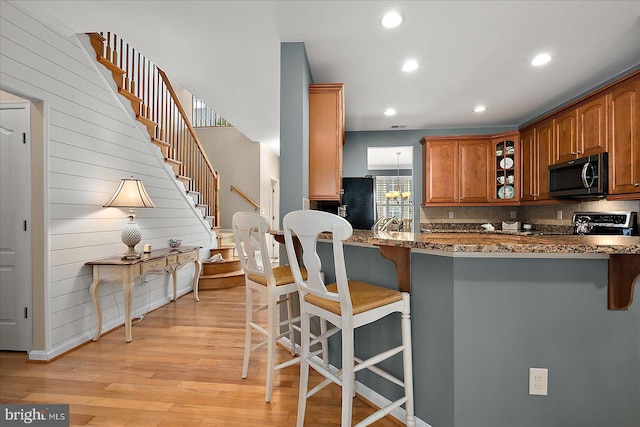 kitchen with stainless steel microwave, glass insert cabinets, dark stone counters, a kitchen breakfast bar, and light wood-style floors