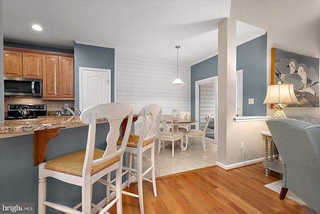 kitchen with electric range, stainless steel microwave, light wood-style floors, a breakfast bar area, and brown cabinetry