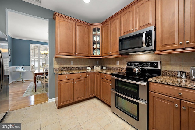 kitchen with backsplash, brown cabinets, stainless steel appliances, and dark stone countertops