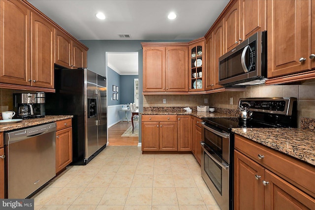 kitchen with backsplash, stainless steel appliances, brown cabinets, and dark stone counters