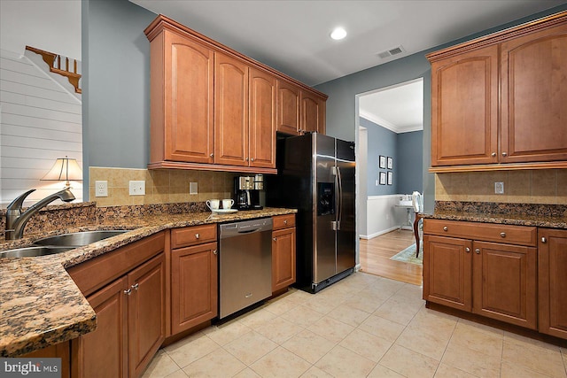 kitchen with brown cabinetry, visible vents, dark stone counters, a sink, and stainless steel appliances