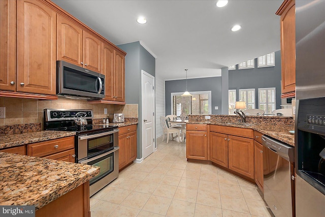 kitchen featuring a sink, appliances with stainless steel finishes, a peninsula, brown cabinetry, and decorative backsplash