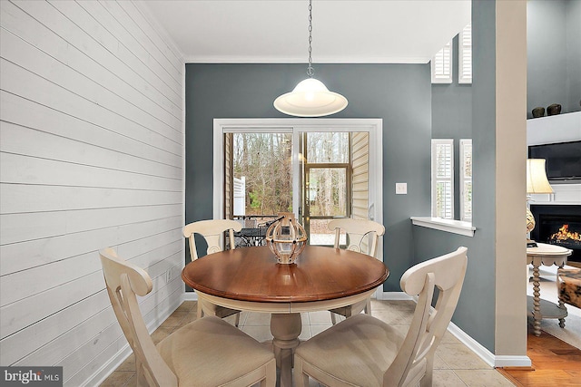 dining space featuring baseboards, wooden walls, a warm lit fireplace, and crown molding