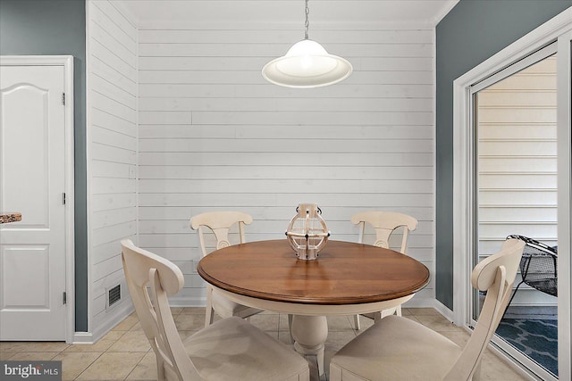 dining room featuring wooden walls, light tile patterned floors, and baseboards