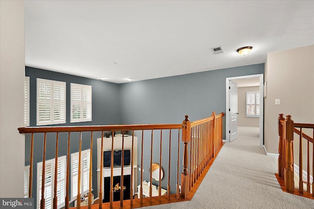 hallway featuring carpet, an upstairs landing, visible vents, and baseboards