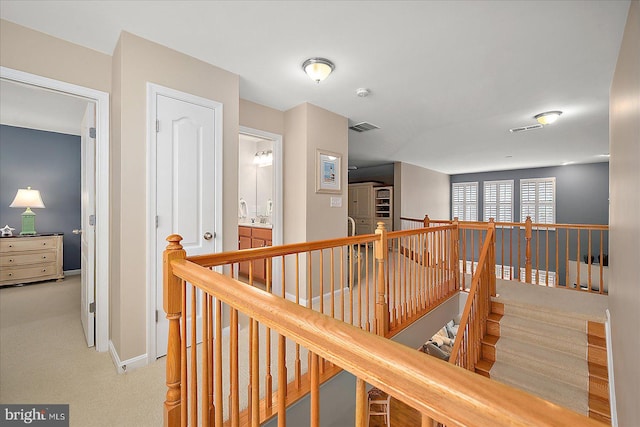 hall with an upstairs landing, visible vents, light carpet, and baseboards