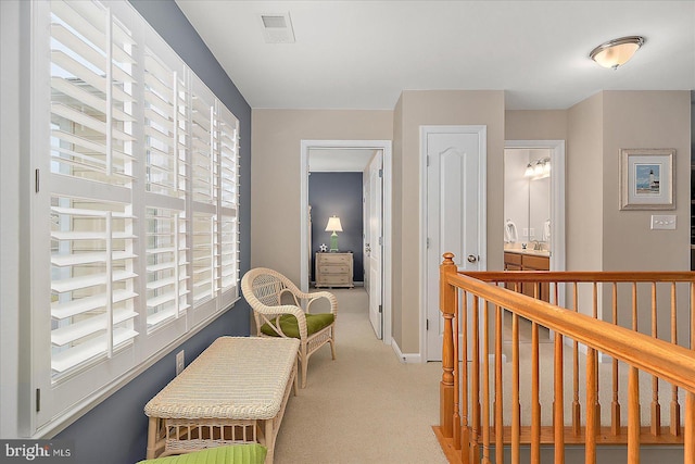 hallway featuring visible vents, baseboards, and light colored carpet