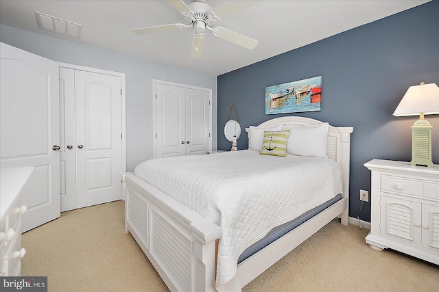 bedroom with a ceiling fan, light colored carpet, visible vents, and multiple closets