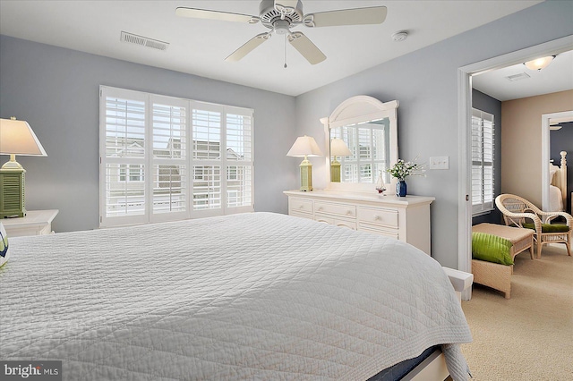 bedroom featuring multiple windows, a ceiling fan, visible vents, and light carpet