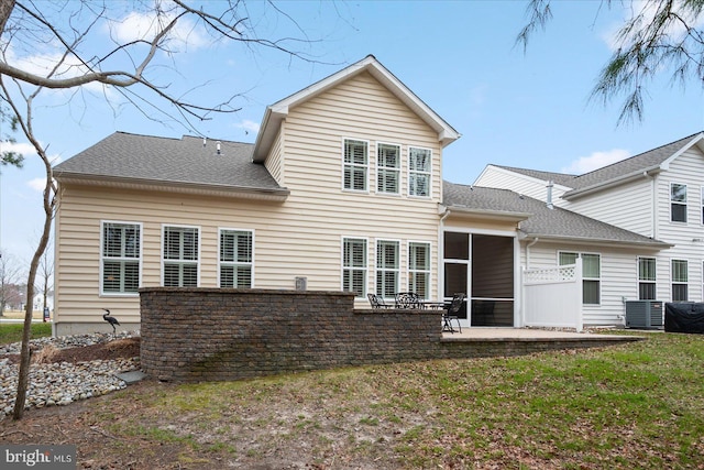 rear view of house with a patio, central AC unit, roof with shingles, a sunroom, and a lawn