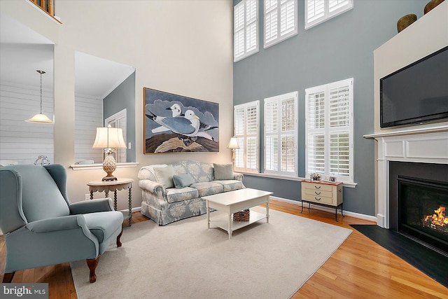 living area with a fireplace with flush hearth, a high ceiling, baseboards, and wood finished floors