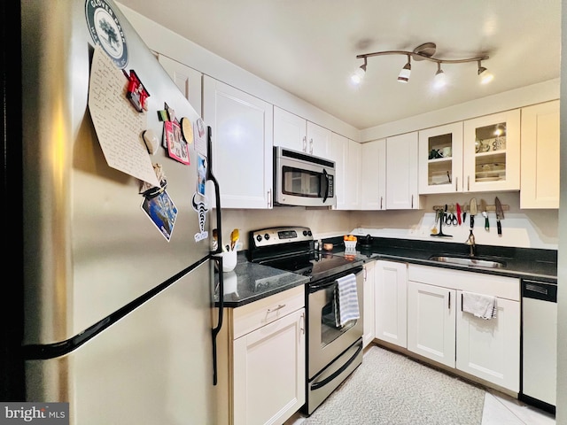 kitchen with a sink, dark countertops, white cabinetry, appliances with stainless steel finishes, and glass insert cabinets