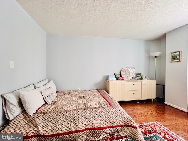 bedroom with baseboards, a textured ceiling, and wood finished floors