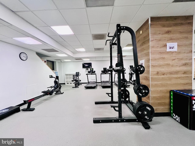 exercise room with visible vents, wood walls, and a drop ceiling