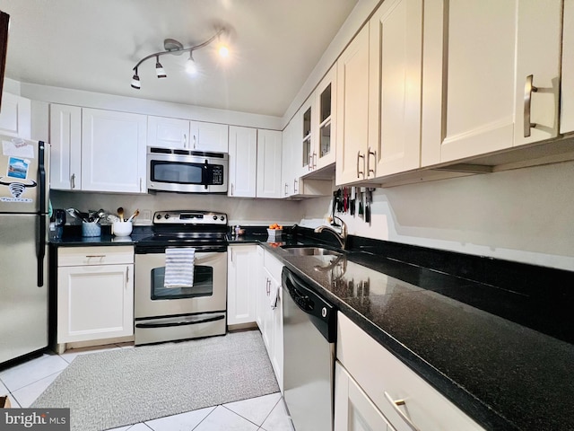 kitchen with light tile patterned flooring, a sink, stainless steel appliances, glass insert cabinets, and white cabinetry