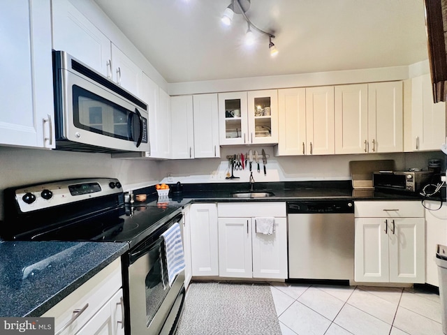 kitchen with a sink, dark countertops, stainless steel appliances, white cabinets, and light tile patterned floors