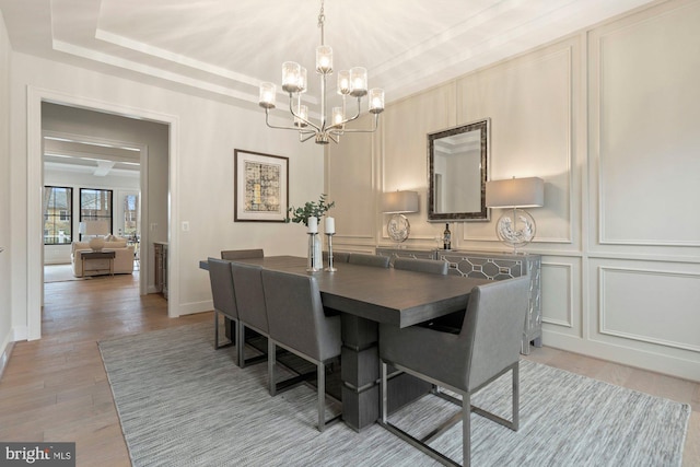 dining room with a raised ceiling, a decorative wall, a notable chandelier, and light wood finished floors