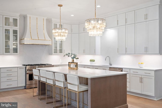 kitchen with custom range hood, a sink, a kitchen island, appliances with stainless steel finishes, and a chandelier