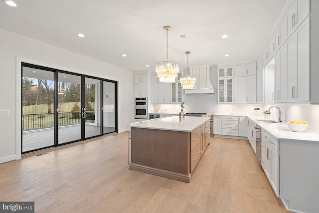 kitchen with premium range hood, a sink, light countertops, light wood-style floors, and a notable chandelier