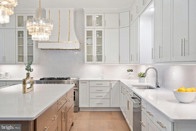 kitchen with a sink, decorative backsplash, stainless steel stove, light wood-style floors, and a notable chandelier