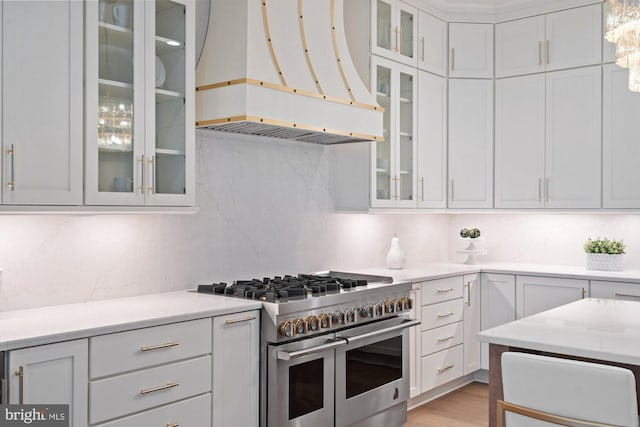 kitchen featuring premium range hood, double oven range, tasteful backsplash, white cabinets, and glass insert cabinets