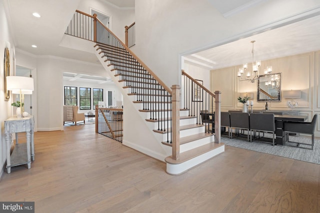 stairway featuring baseboards, an inviting chandelier, wood finished floors, and crown molding