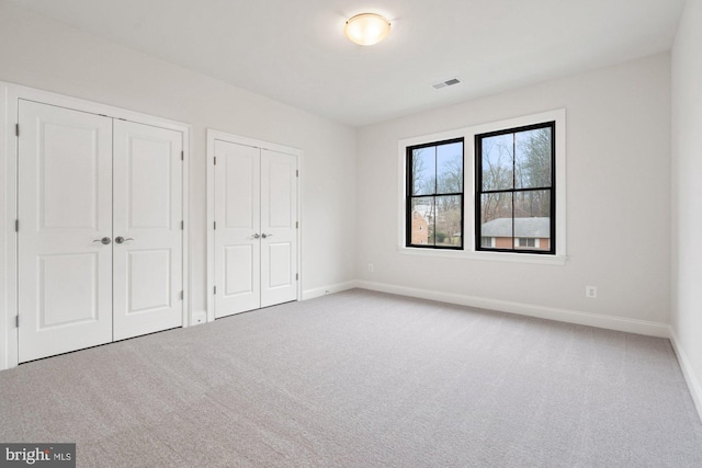 unfurnished bedroom featuring visible vents, carpet, multiple closets, and baseboards